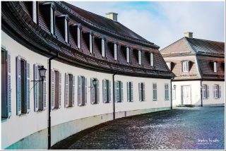 Dieses Foto ist als kostenloser Download (ohne Rand und Signatur) im Originalformat oder als Print zum Kauf/Mieten in meinem Shop auf <a href="https://butlaix.de/produkt/fotografie-schloss-solitude-no-5/" target="_blank" rel="noreferrer noopener" >BUTLAIX_media</a> verfügbar. Historisches Gebäude mit geschwungener Fassade, cremefarbenen Wänden, grauen Fensterläden und Mansarddach mit Gauben. Kopfsteinpflaster im Vordergrund, alte Straßenlaterne an der Wand.
