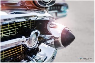 Dieses Foto ist als kostenloser Download (ohne Rand und Signatur) im Originalformat oder als Print zum Kauf/Mieten in meinem Shop auf <a href="https://butlaix.de/produkt/fotografie-chevrolet-bel-air-no-1/" target="_blank" rel="noreferrer noopener" >BUTLAIX_media</a> verfügbar. Das Bild zeigt die Nahaufnahme eines klassischen Autostoßfängers aus Chrom. Zu sehen sind glänzende Details wie eine runde Lampe, das charakteristische, raketenförmige Design und ein Teil des Kühlergrills im Retro-Stil, der an Autos der 1950er erinnert.